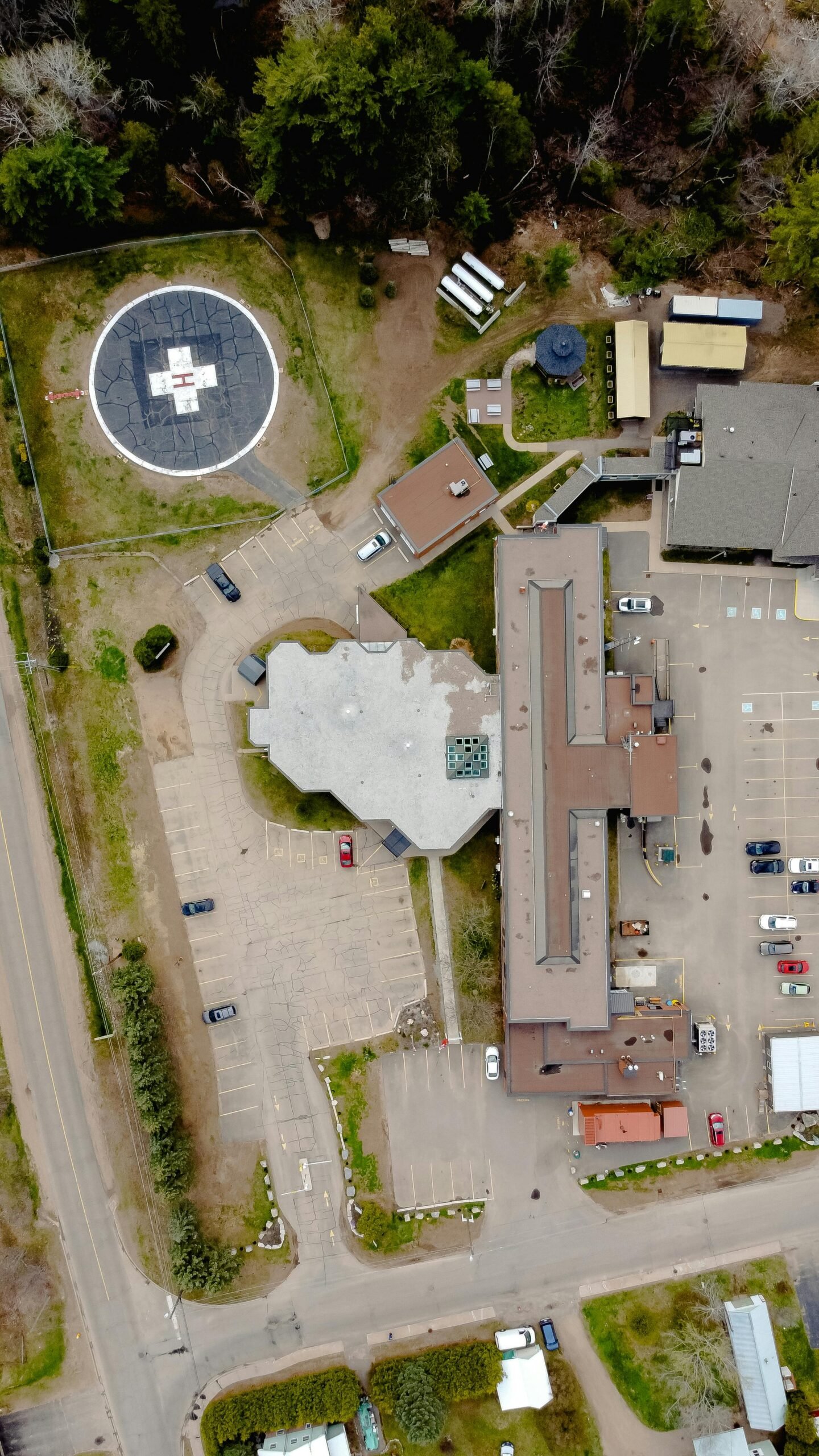 Aerial view of large building complex with adjacent helipad and parking lot.